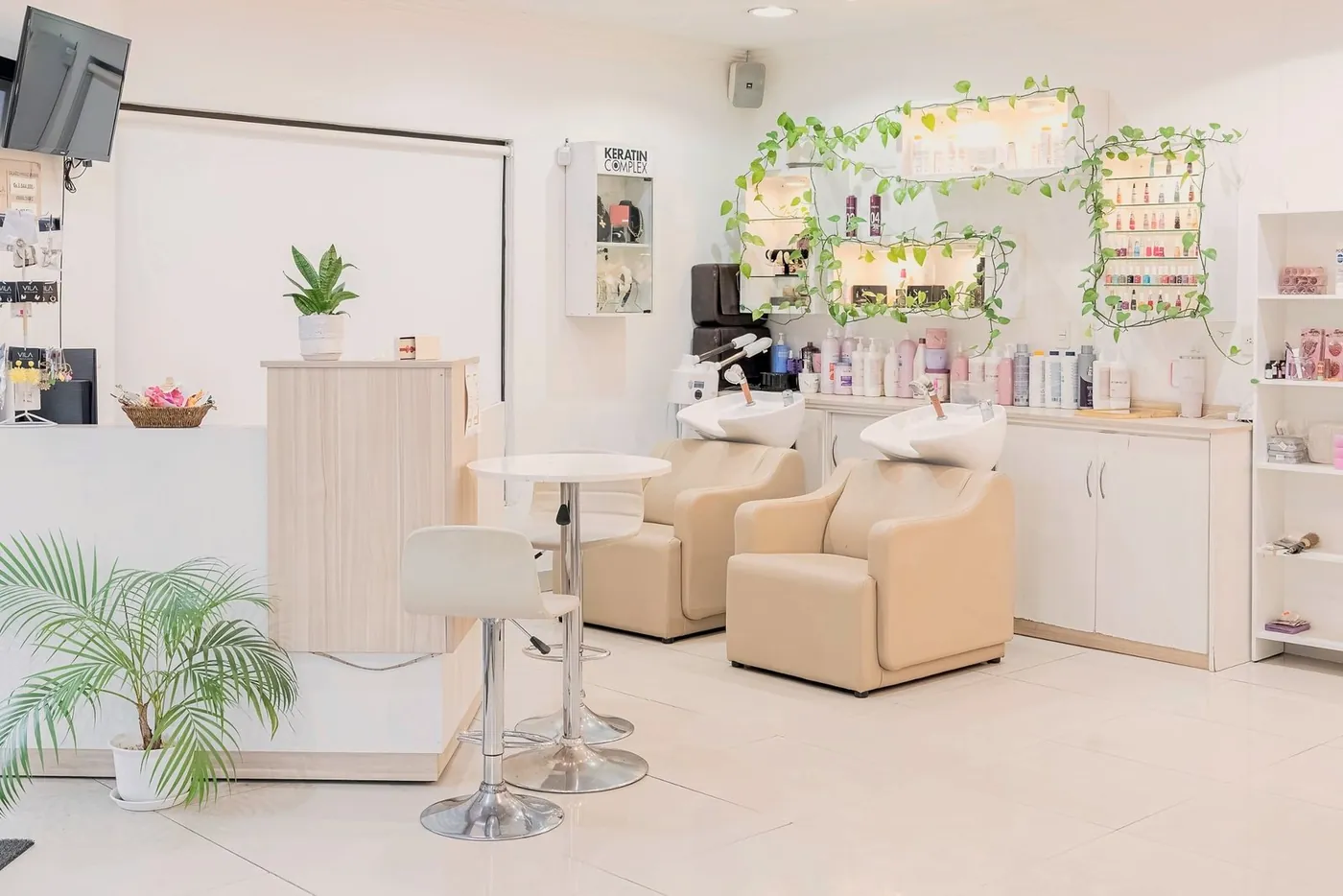 Recepción con mesa alta, palmera y sillones de lavado al fondo